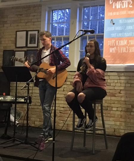 two students on stage singing and playing the guitar