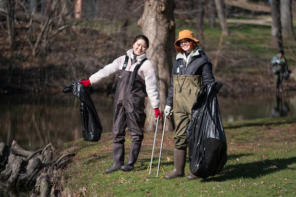 两个穿着服务生裤子的学生在清理完Coldbrook Creek后拿着垃圾袋